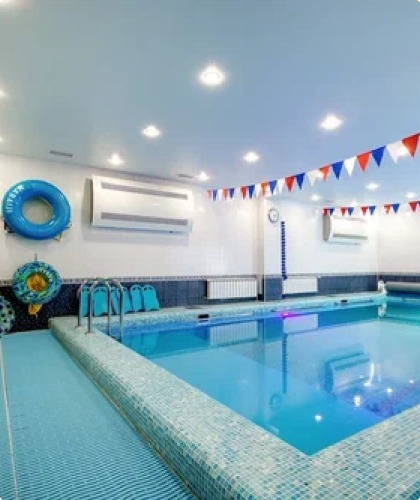 Внутренний бассейн с мозаичной отделкой, поручнями для спуска в воду и разноцветными флажками, натянутыми под потолком.