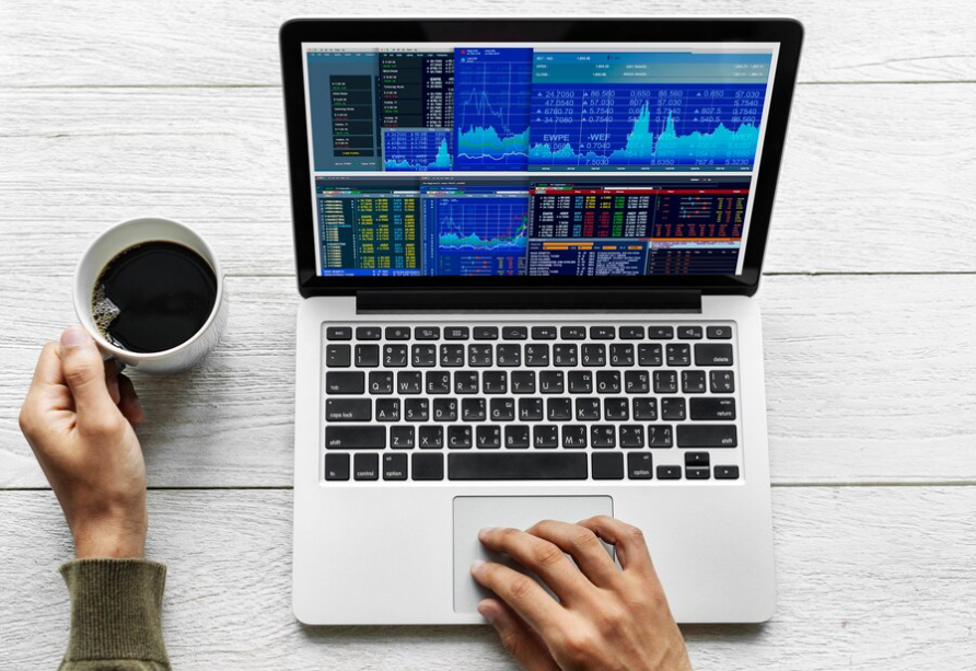 Scalping vs. Intraday Trading: A person with a cup of coffee and a laptop is looking at price charts for intraday trading.