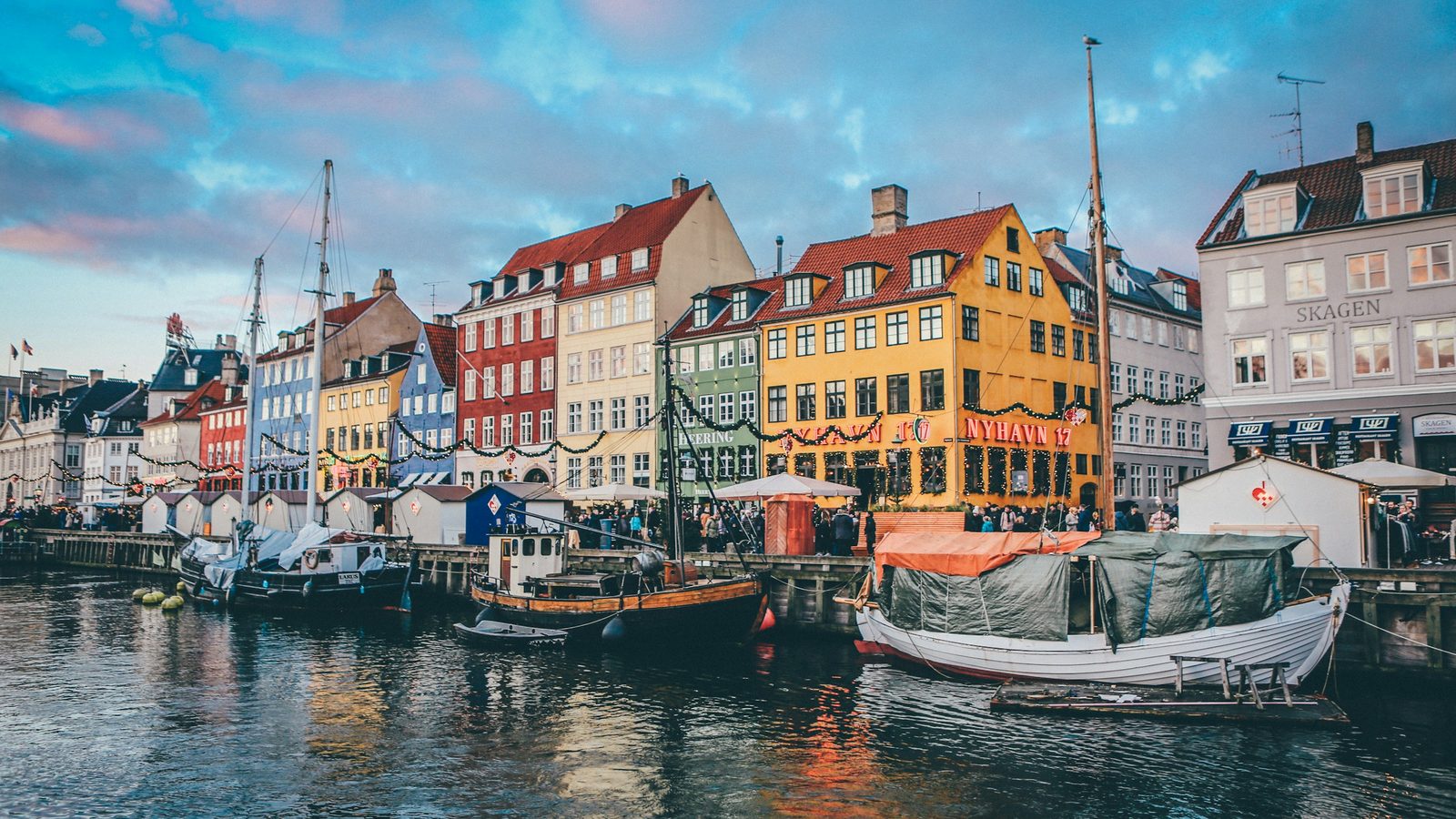 Wooden boats moored in the Nyhavn canal in front of colourful gabled houses and Christmas stalls, Copenhagen