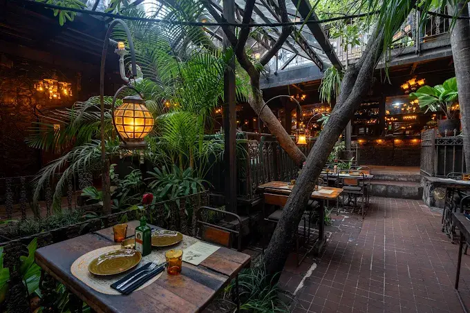 The lush, vintage-inspired garden courtyard at La Favela Seminyak, featuring antique lighting and tropical greenery for an eclectic night out.