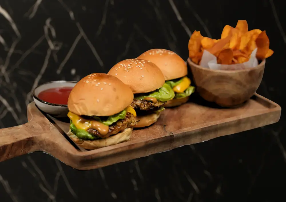 A close-up of the signature slider burger, a top choice for a halal burger in Ubud, served with sweet potato chips and dipping sauce on a wooden board.