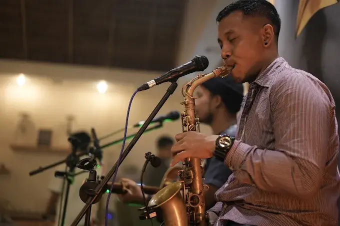 A passionate close-up shot of a musician playing the saxophone into a microphone during an intimate acoustic set at a cozy lounge. Catching these live jazz sessions is definitely the best event in Bali for a chill vibe.