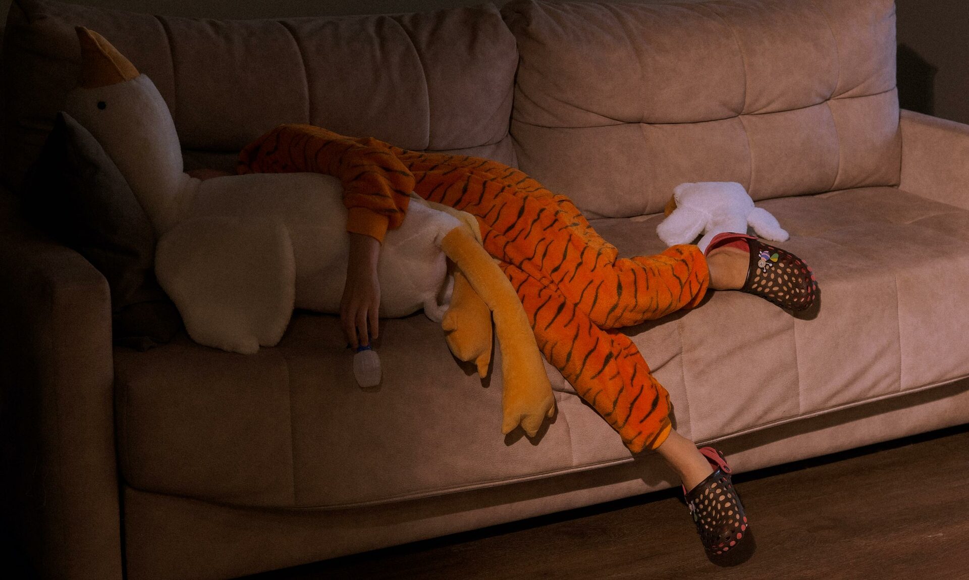 Ребёнок в тигровой пижаме лежит на диване в обнимку с плюшевой игрушкой гуся