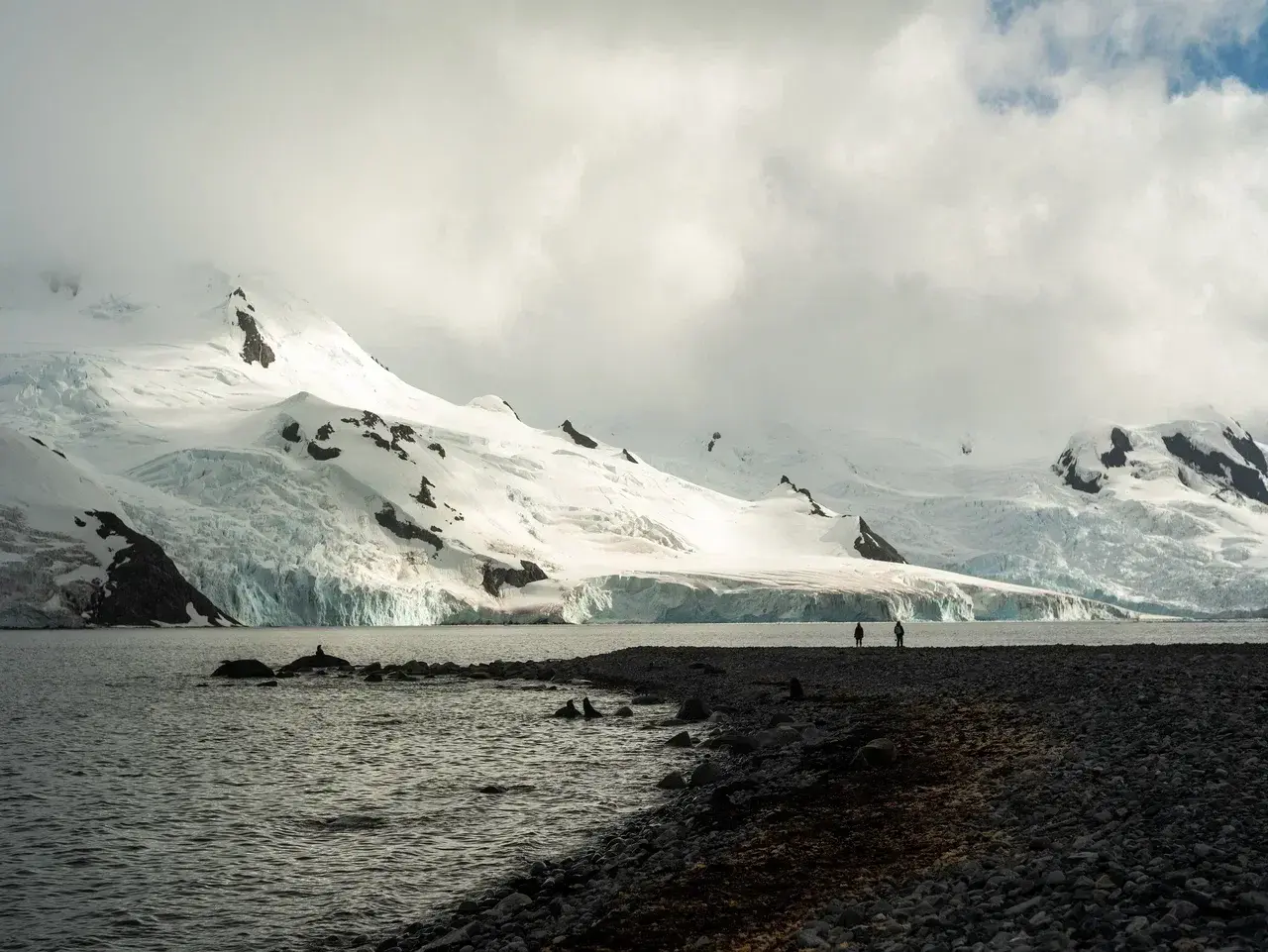 Snow-covered mountains and glaciers along the Antarctic coast during a trip to Antarctica with travelers exploring the remote polar landscape.
