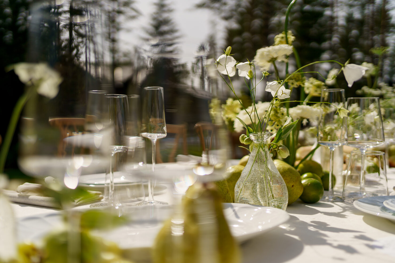 Сервировка свадебного стола на открытом воздухе: стеклянные бокалы, ваза с белыми цветами и композиция из груш и лаймов — летний банкет на загородной свадьбе в Санкт-Петербурге от Global Wedding &amp; Event.