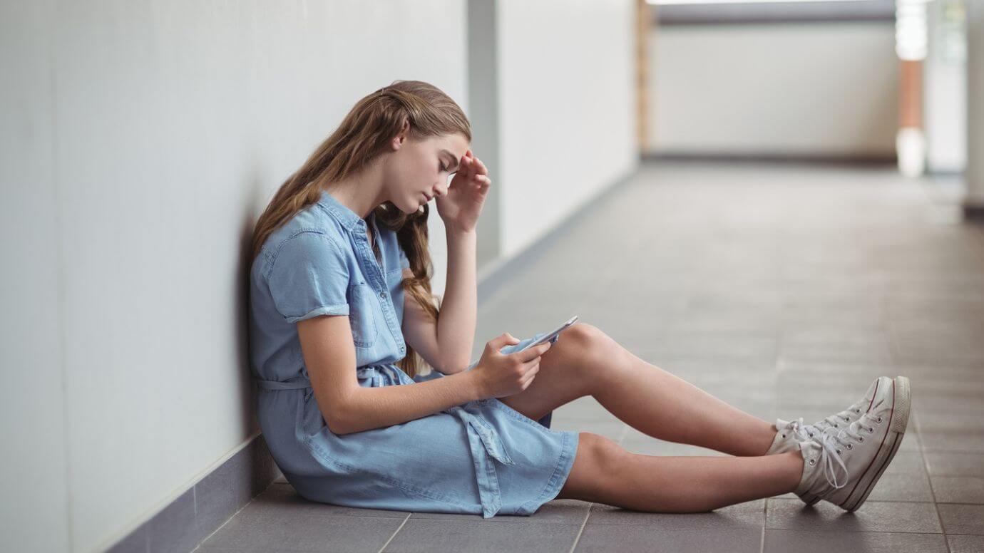 Sad young brunette woman sitting on the floor, engrossed in her phone