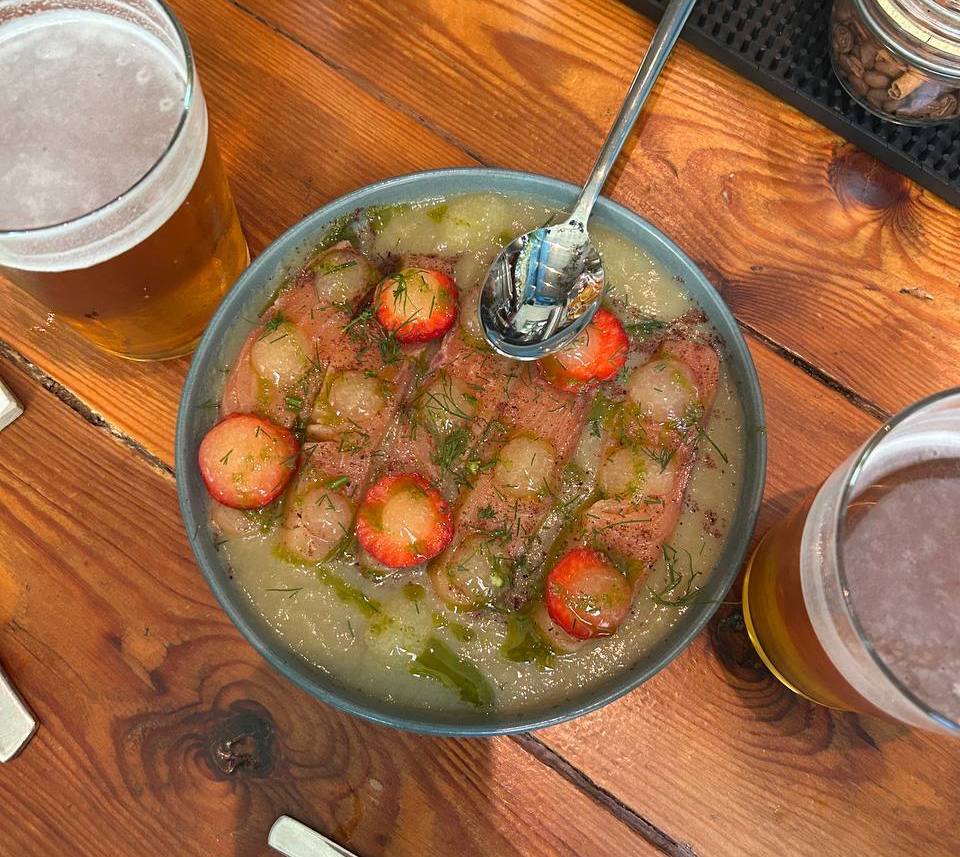 Cold dish with thin pinkish slices in a clear broth, with dill, sumac and fresh strawberries at Sensi