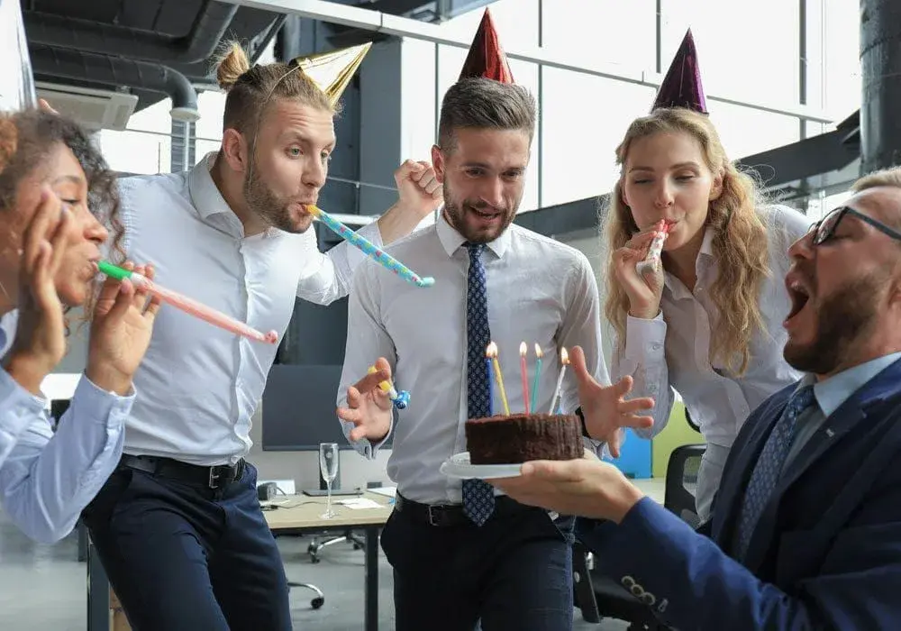 Коллеги в офисе празднуют день бухгалтера, на столе торт Зебра и чай, радостная атмосфера.