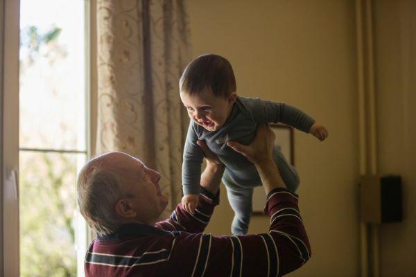 Un nonno alza al cielo il suo nipotino e lo fa sorridere