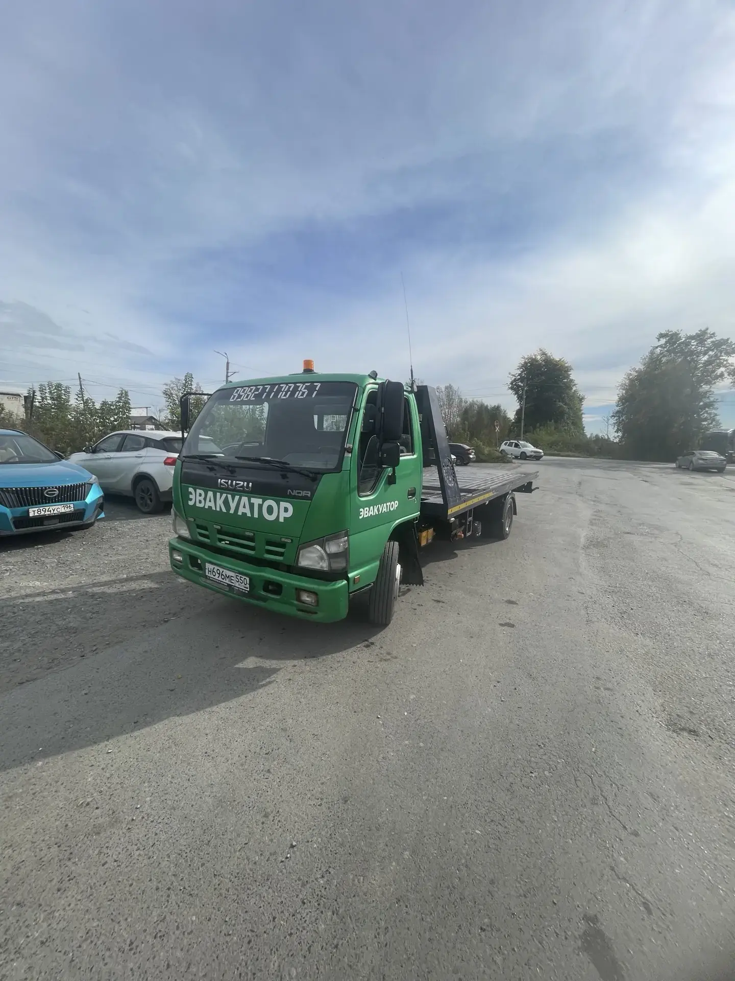 Зелёный эвакуатор Isuzu NOR на стоянке в солнечный день, вид спереди