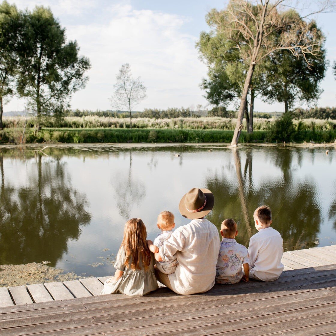 A family sitting on the boardwalk over the water at Ostrov Glamping