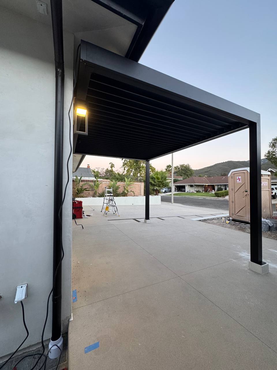 View along the house wall beneath the completed black pergola and louvered roof.