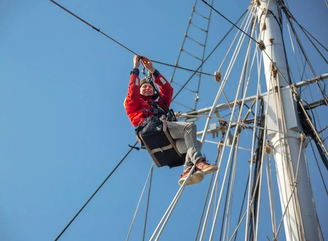 Participant learning traditional seamanship while climbing the rigging on a tall ship during a sailing expedition