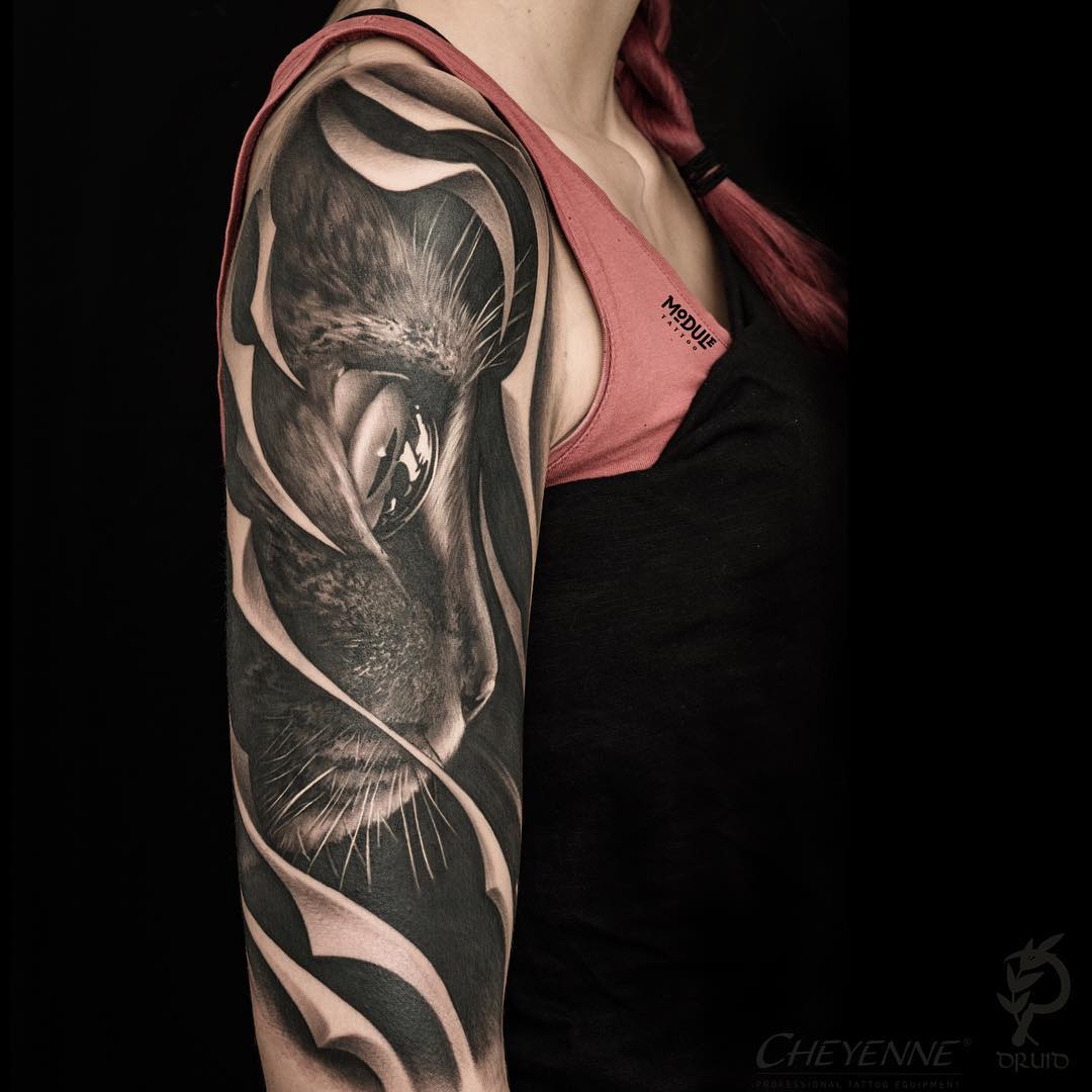 A professional black and grey realism shoulder tattoo of a cat's face with a highly detailed eye, integrated with abstract flowing shapes on a female arm, Los Angeles