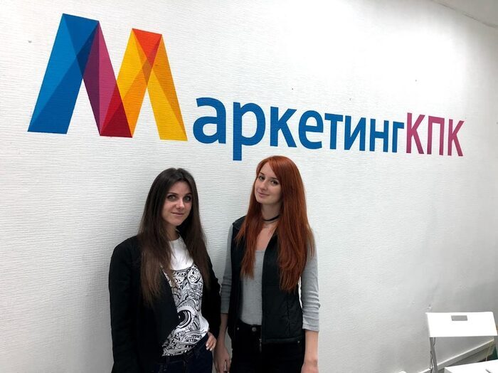 Две выпускницы программы у логотипа МаркетингКПК