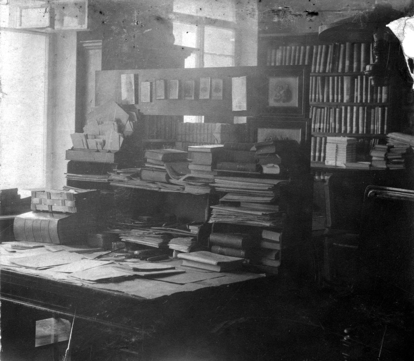 Письменный стол со стопками бумаг и книг, книжные полки в кабинете, старая фотография