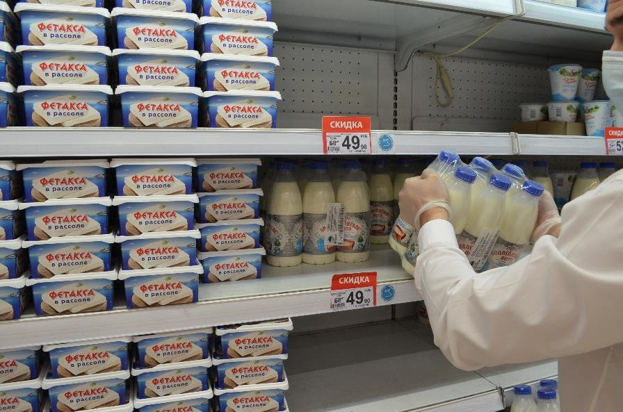 Сотрудник выставляет молочную продукцию на полки торгового зала