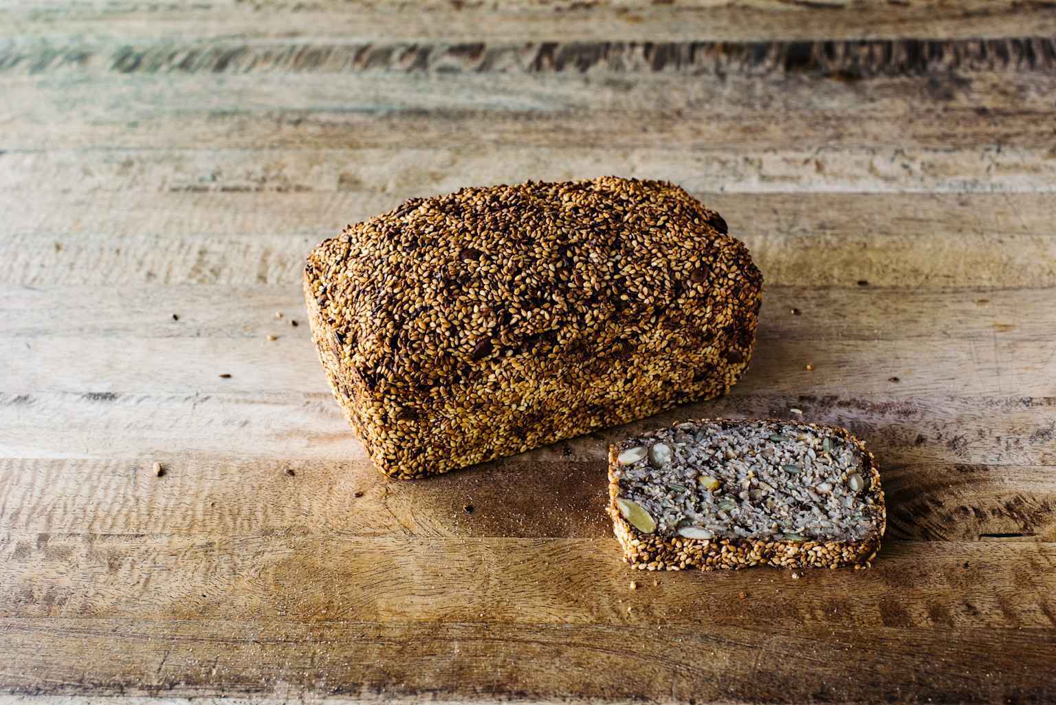 A hemp seed loaf, rich in varied seeds and grains, with a thick sesame seed crust, presented on a wooden surface