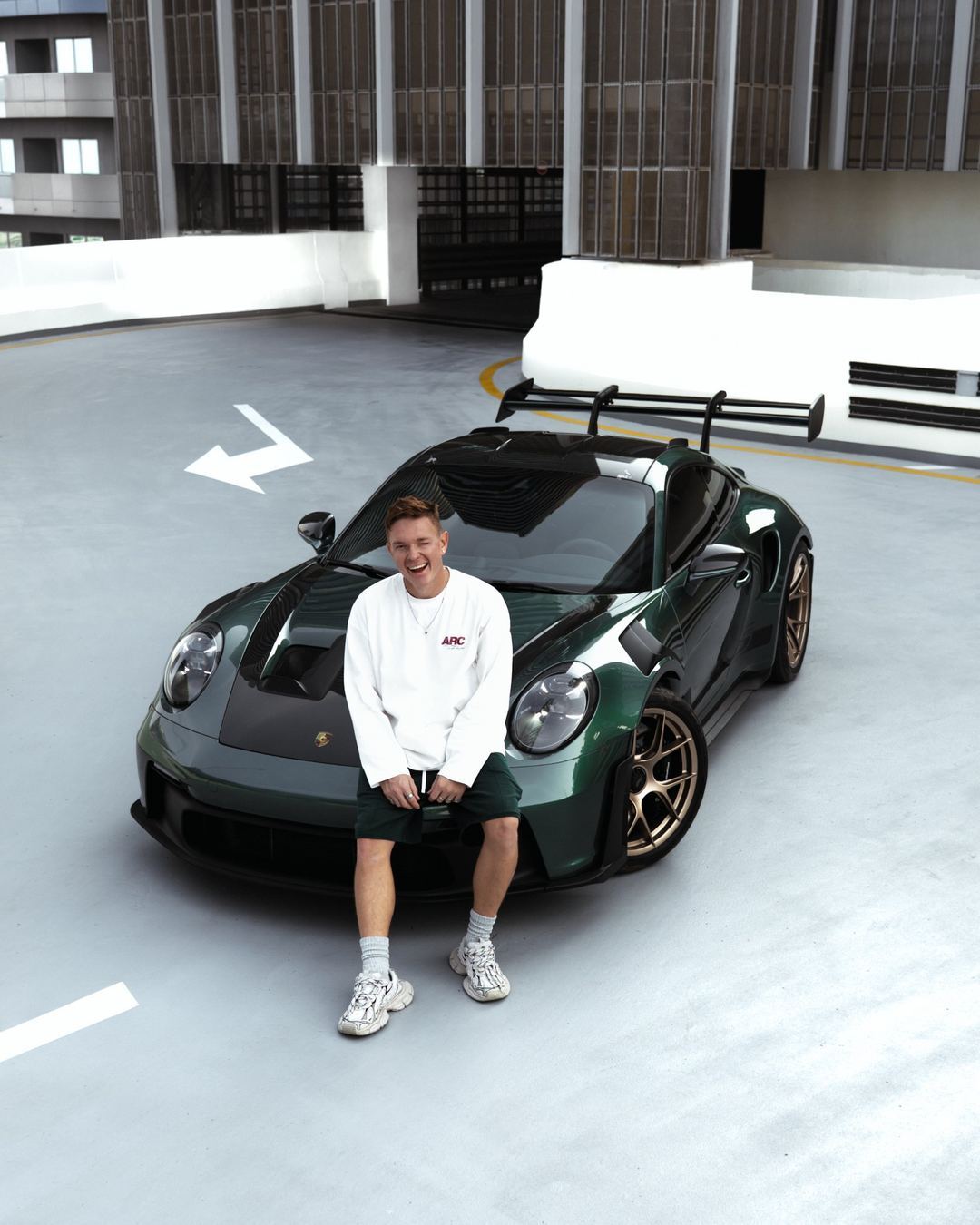 Ivan Petrov laughing, sitting on the front of a green Porsche 911 GT3 RS on a Dubai rooftop
