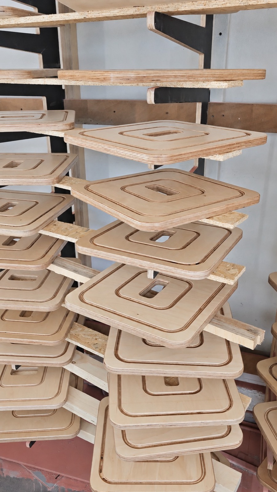 Identical plywood seat tops stacked on a drying rack