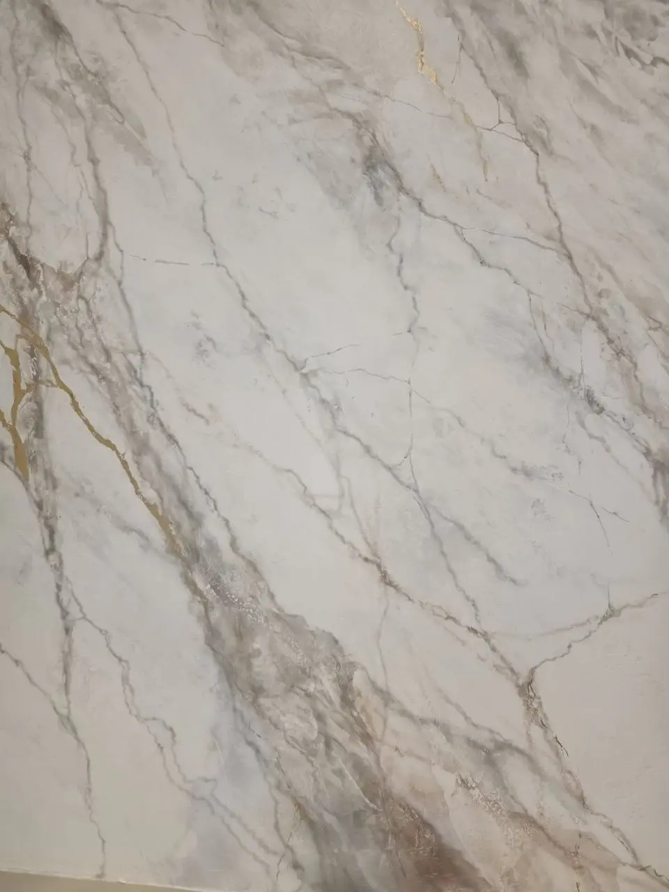 Close-up of hand-applied Venetian plaster with gray, taupe, and metallic gold veining.