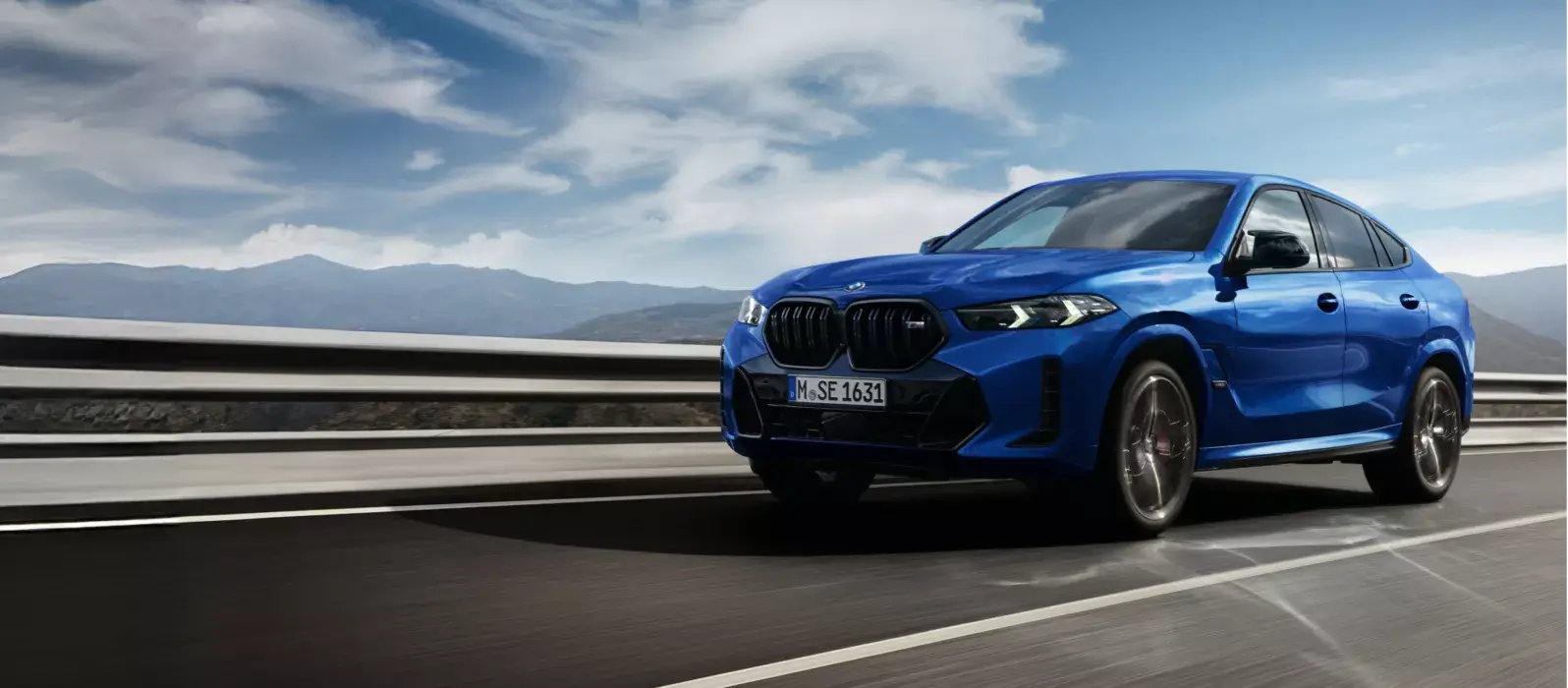 BMW X6 едет по скоростной трассе на фоне горной панорамы