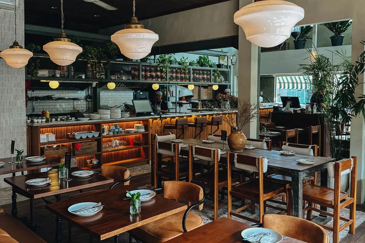 A warm and cozy interior view of Wild Habit Pizza, featuring wooden dining tables and an authentic pizza oven in the background, making it a great spot to share pizza and some of the best pasta in Seminyak with friends.