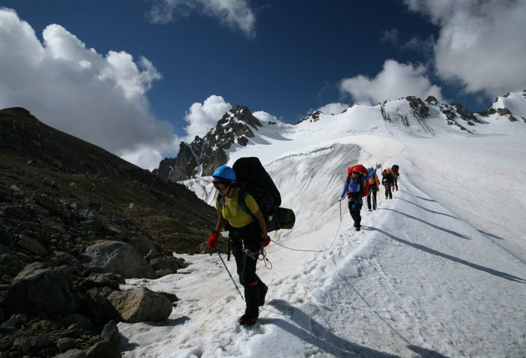 Roped climbers with heavy rucksacks on a snowy ridge