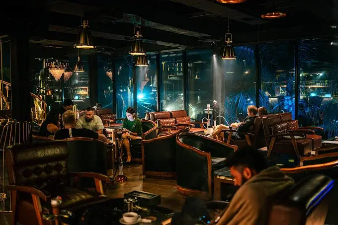 A lively evening crowd relaxing on cozy leather armchairs under moody blue lighting at Hubble, a popular casual hookah spot in Canggu, Bali.