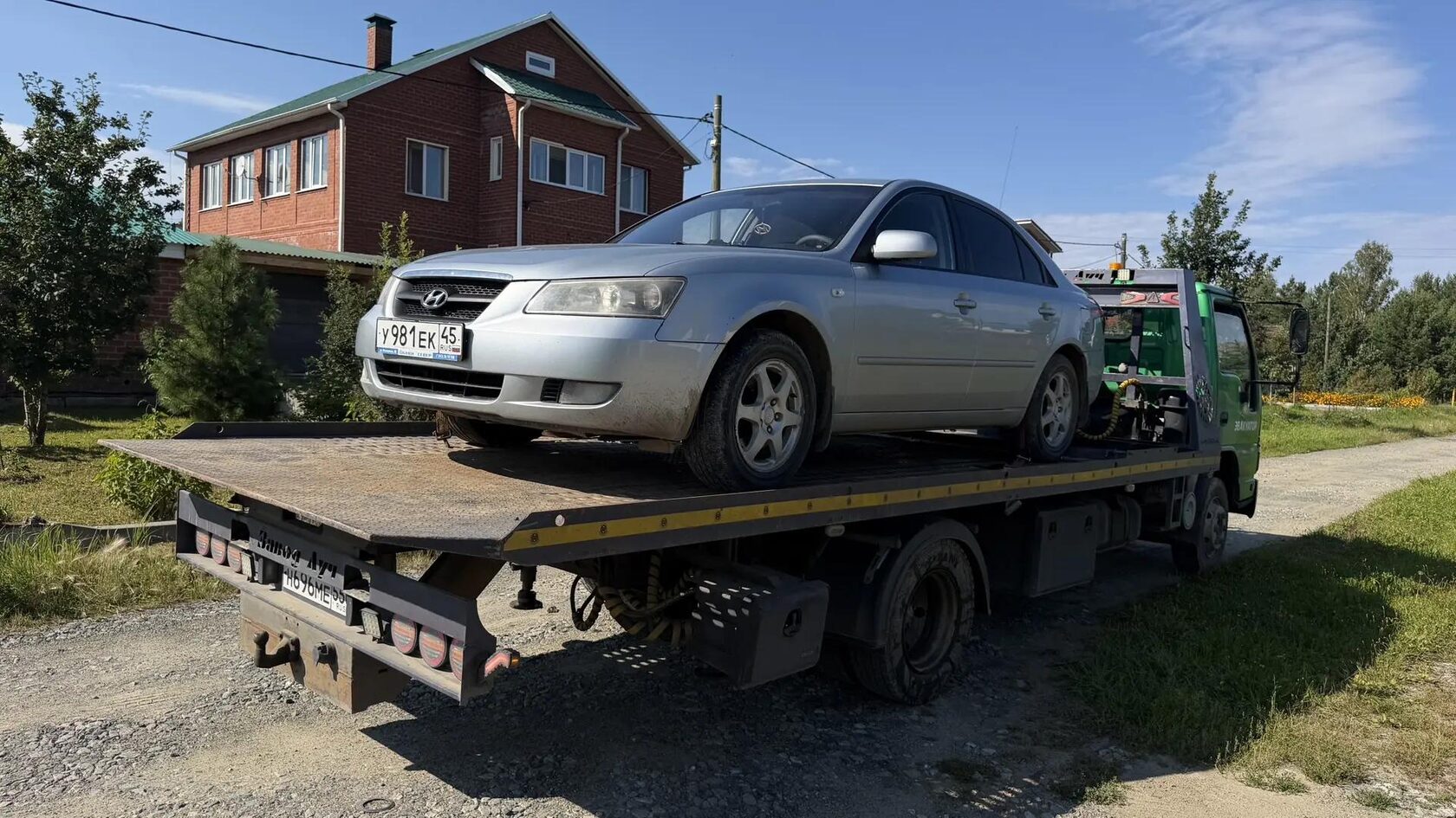 Седан Hyundai Accent на платформе эвакуатора у деревянного дома