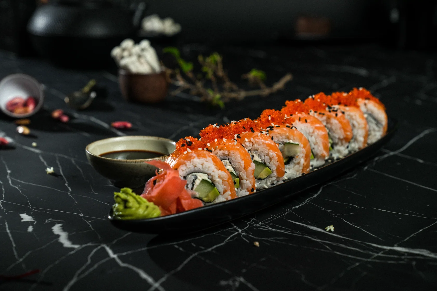 Philadelphia sushi roll with salmon, avocado, cucumber and red tobiko served on a black plate