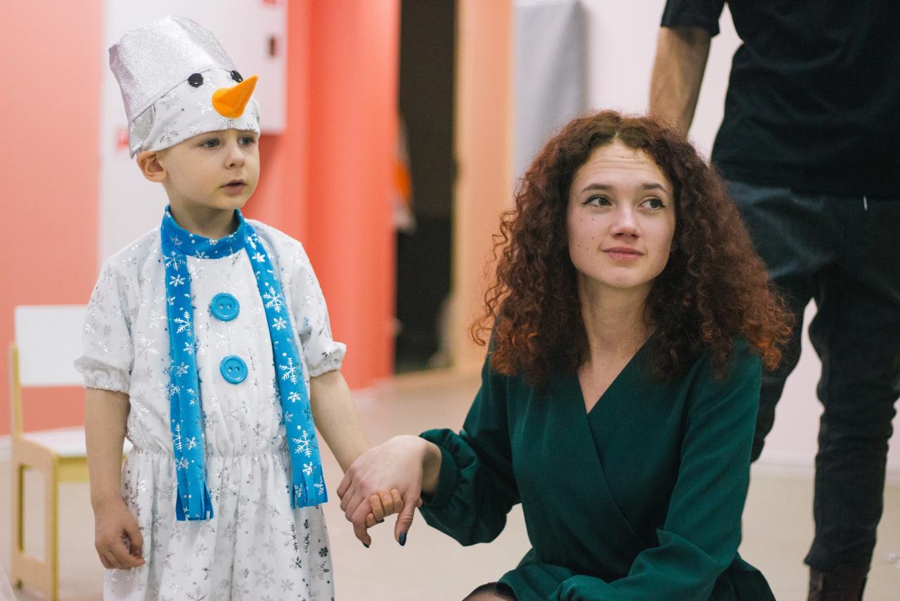 Ребёнок в костюме снеговика держит за руку воспитателя во время утренника в детском саду