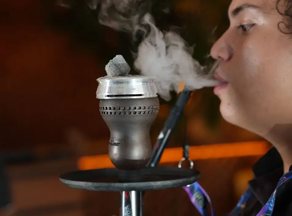  A person exhaling thick white smoke clouds from a hookah, indicating a successful setup and optimal heat management.