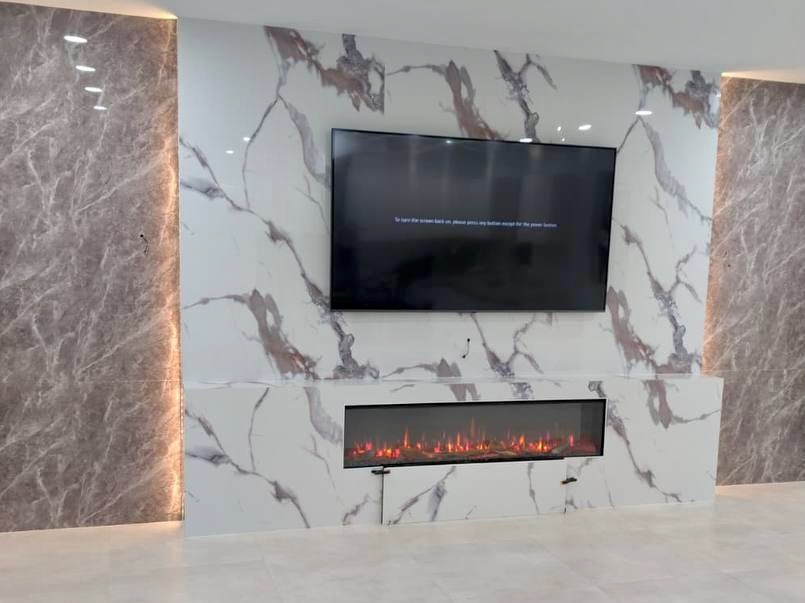 Completed marble-look media wall in a Miami home with an electric fireplace, mounted television, contrasting side panels, and ambient lighting.
