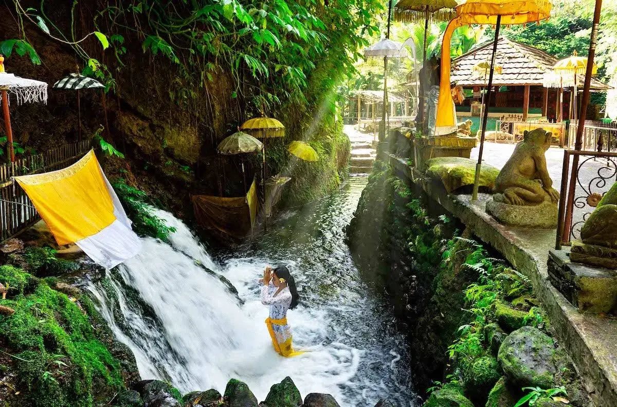 A woman performing a traditional water purification ritual under a serene spring waterfall at Sebatu Holy Spring, offering a peaceful spiritual escape during an Ubud getaway.