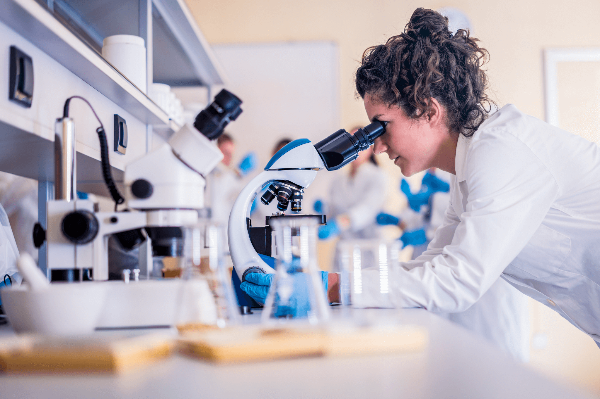 Frau in Laborkittel blickt in einem Labor durch ein Mikroskop