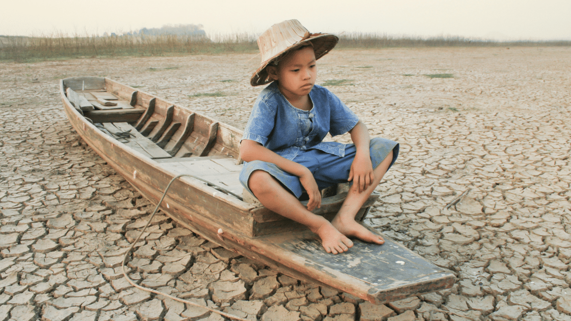 criança sentada em uma barco, em uma terra seca. Metáfora para as crises climáticas.
