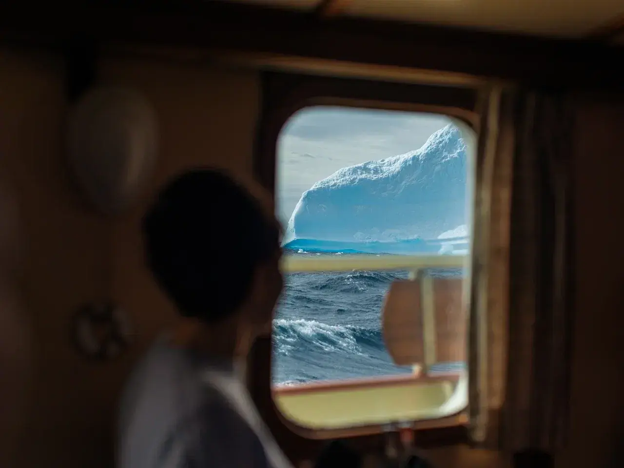 View of a towering Antarctic iceberg through the cabin window of a sailing yacht during an expedition.