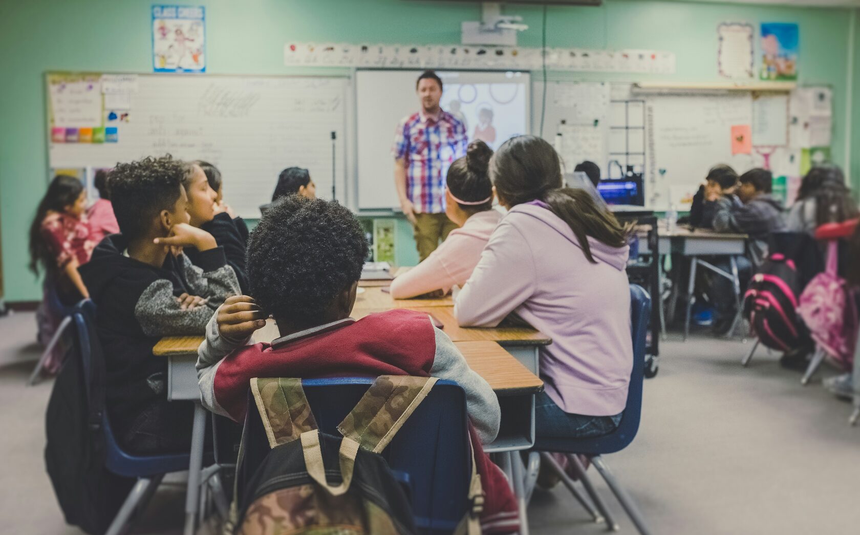 Students in a classroom look at their teacher at the front of class