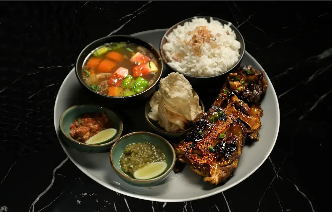 Grilled sweet and spicy beef oxtail served with rice, vegetable soup, crackers, lime, and sambal