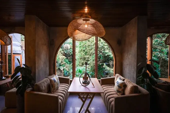 A cozy private alcove at Eden Hookah Club Ubud, with comfortable velvet sofas and a single shisha setup overlooking a lush tropical garden through an arched window. Experience tranquil clouds in one of the best hookah bars in Bali.