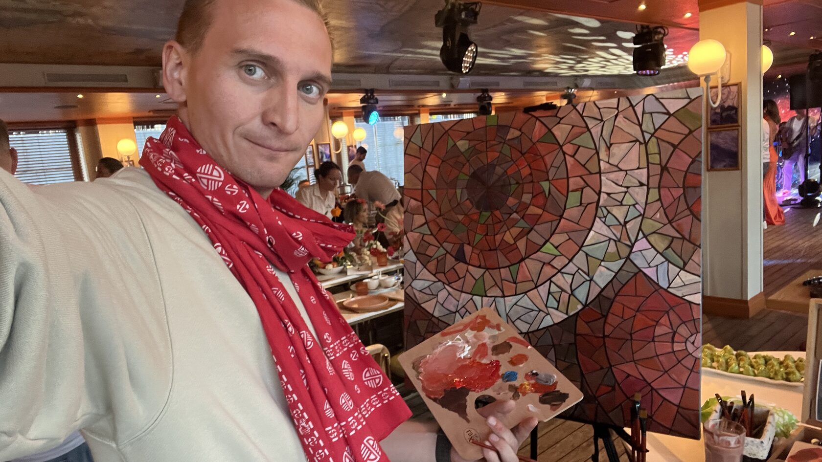 Художник ArtWorker с палитрой в руках на фоне готовой работы на мероприятии